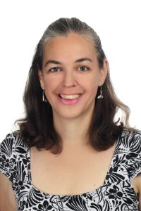 Head and shoulders shot of a smiling cis white female with shoulder-length dark hair and a black and white top
